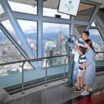 kelaurga sedang memerhatikan pemandangan bandaraya kuala lumpur dari kl tower observation deck melalui teropong yg tersedia